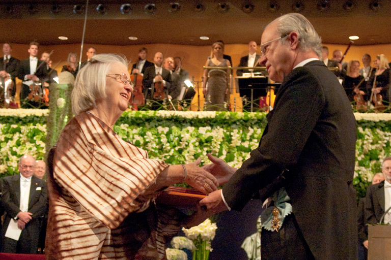 An archival image of Elinor Ostrom (left, in a brightly patterned traditional kaftan) receiving her Nobel Prize during the ceremony.